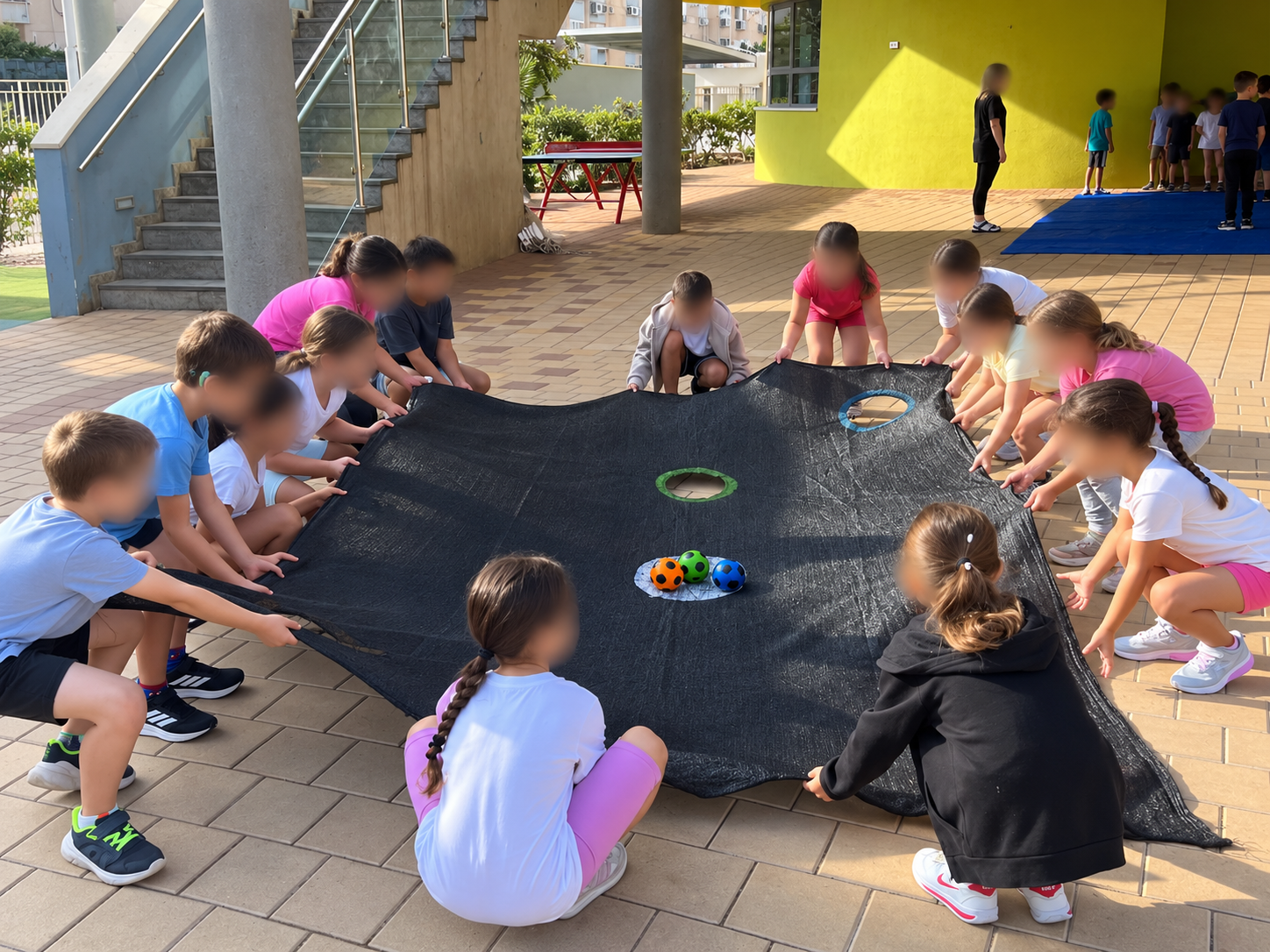 קבוצת ילדים מחזיקה יריעה ומכוונת יחד כדורים, עם פנים מטושטשות